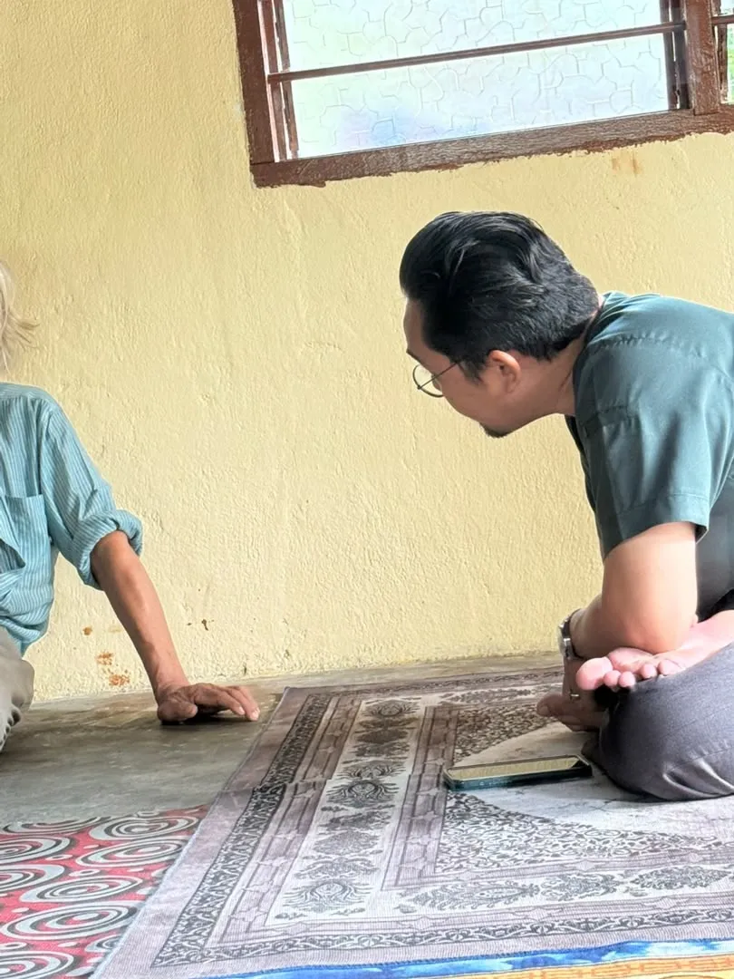 Dr Hafiz melutut di atas tikar untuk mendengar seorang pak cik semasa lawatan ke rumah.